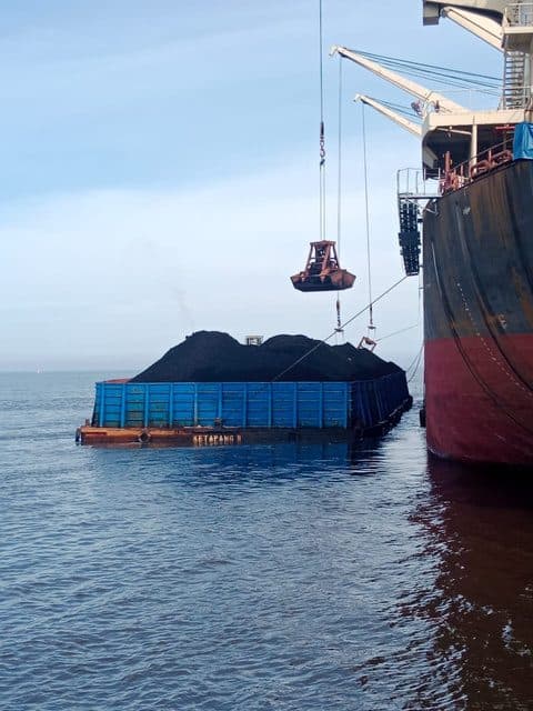 Grab crane memindahkan batu bara dari tongkang ke kapal induk saat transhipment di anchorage